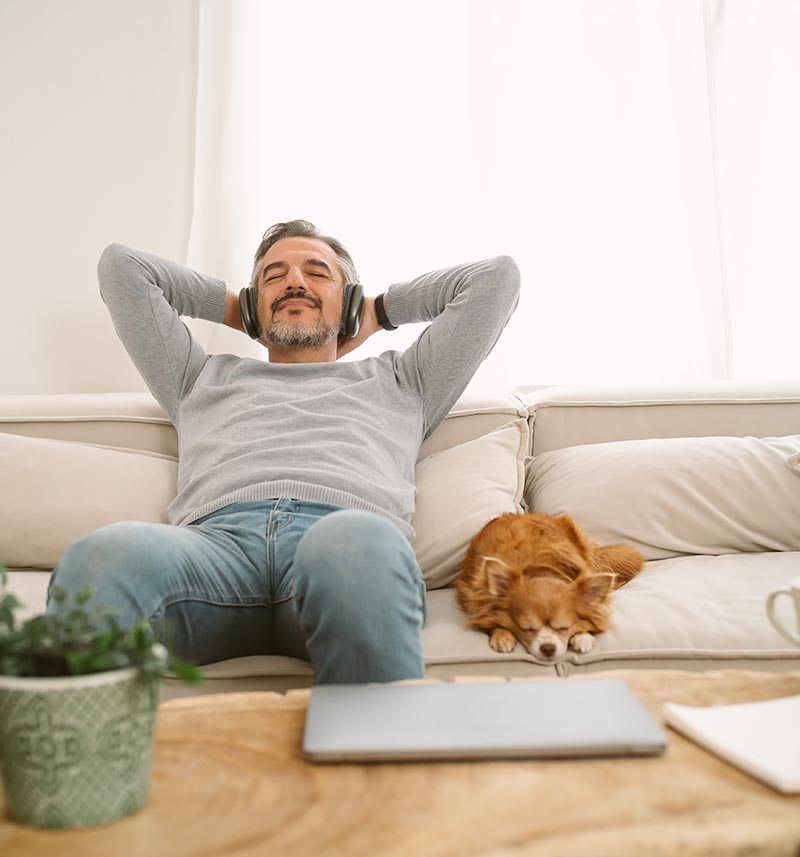 Mann mittleren Alters entspannt sich nach Augenlaserbehandlung auf dem Sofa und hört beruhigende Musik zur Unterstützung der Heilung.