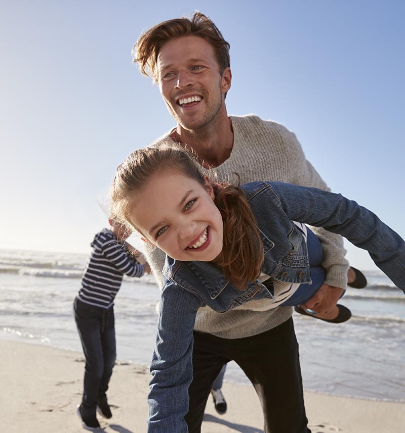Vater und zwei Kinder genießen einen Winterspaziergang am Strand – eine klare Sicht ohne Brille dank Augenlasern.